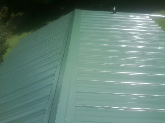 New green metal panels meeting at the ridge of a roof — Flat Roof Repair work by our crew in Fort Worth