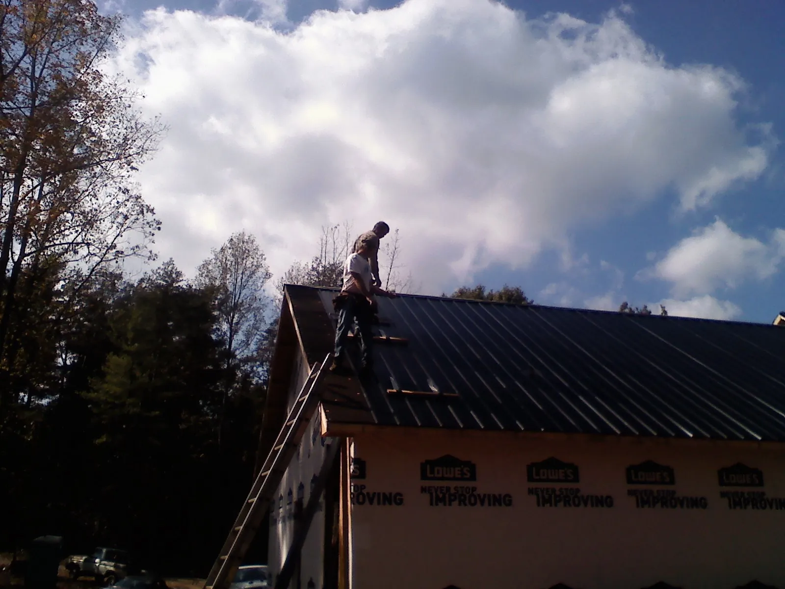 Roofer fastening dark metal panels high against a cloudy sky, from a Roof Inspection job in Fort Worth