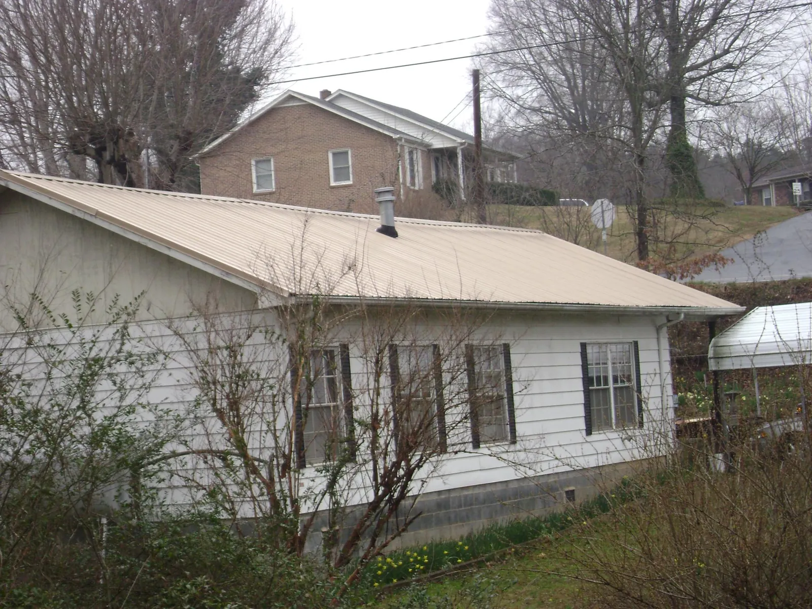 Tan metal roof on a white sided house set into a hillside — Commercial Roofing by Roofing Brothers in Fort Worth
