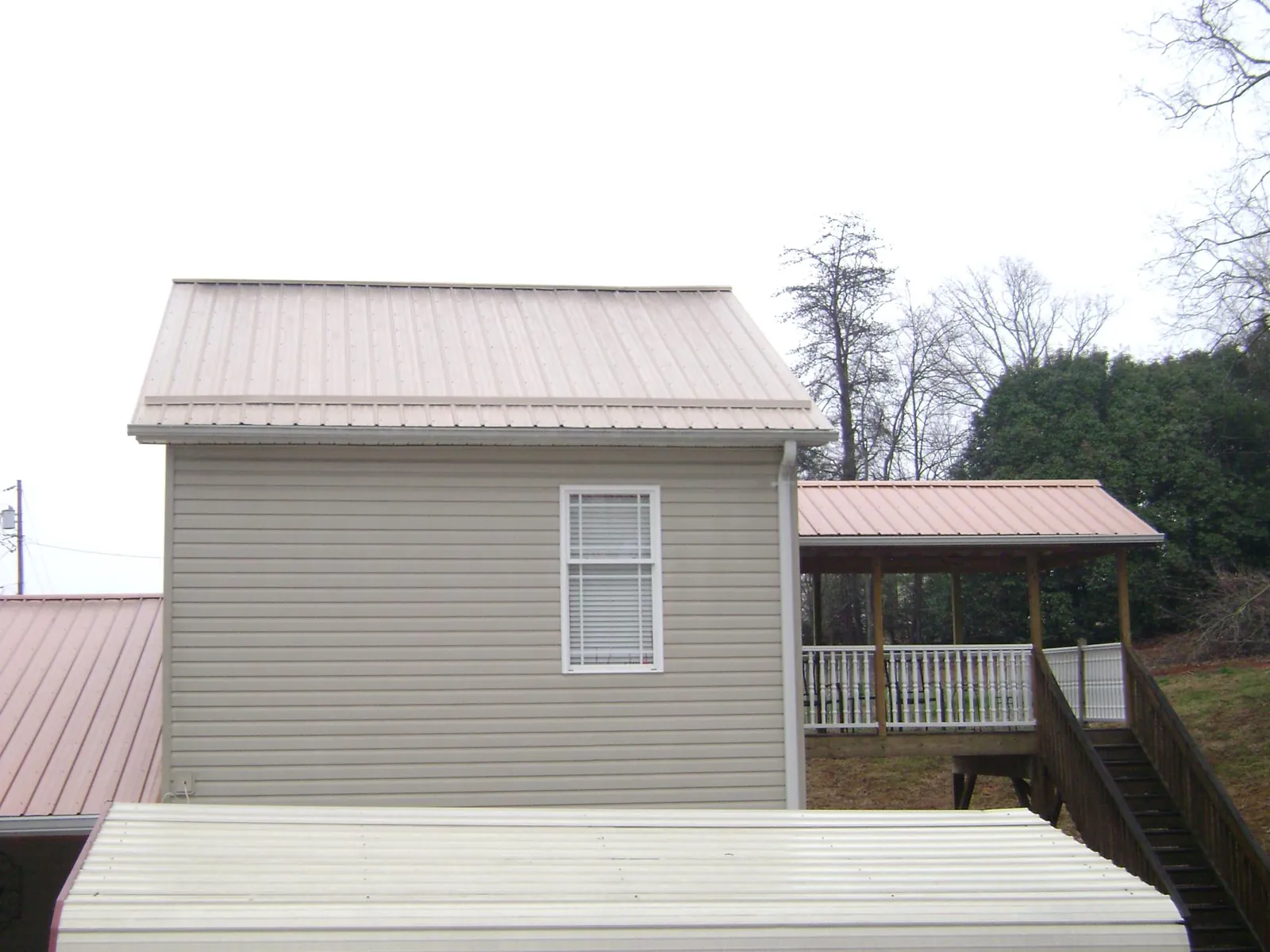 Tan metal roofs on a two story addition and attached porch, from a Roof Replacement job in Fort Worth